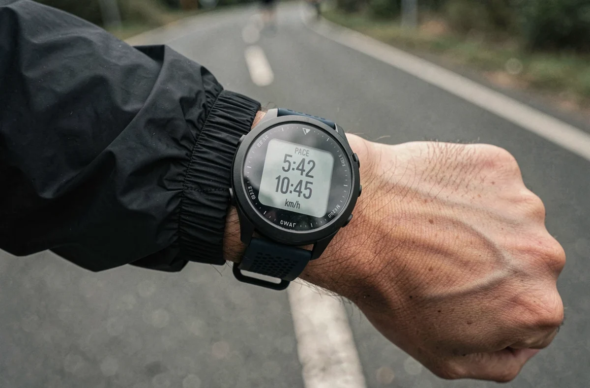 Gros plan sur une montre GPS de course affichant l'allure en min par kilomètre et la vitesse en km/h pendant un footing