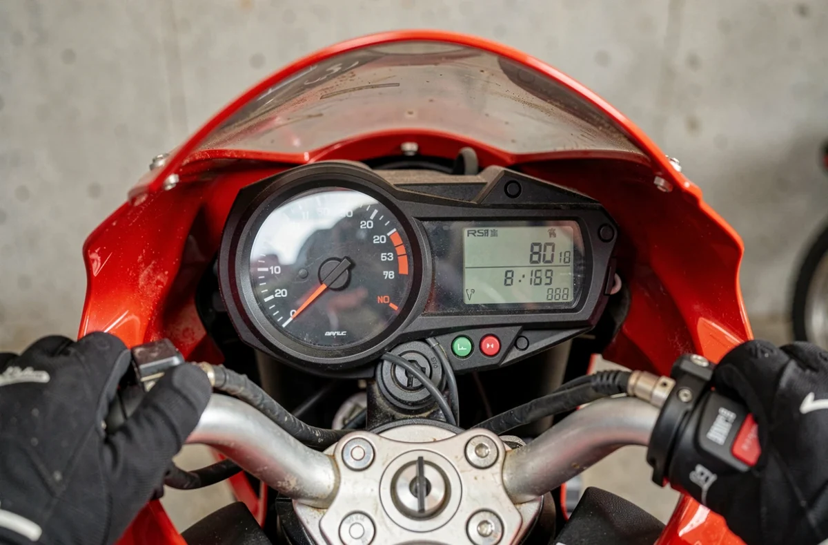 Gros plan sur le tableau de bord et le compteur de vitesse d'une Aprilia RS 125 avec mains gantées sur le guidon